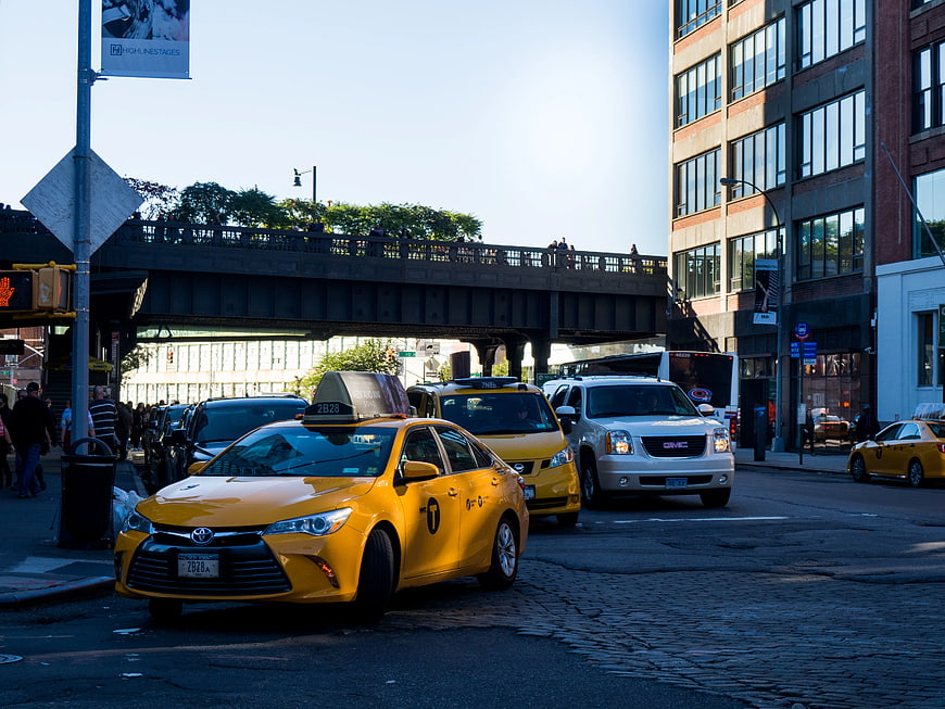 Yellow Taxi Cab on Urban Street Under Elevated Train Tracks