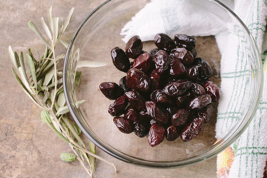 Top view of black olives in glass bowl with olive branch