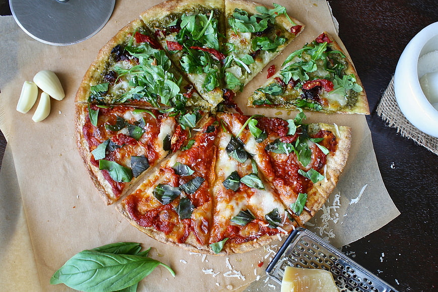 Flat lay of two sliced pizzas with fresh basil and garlic