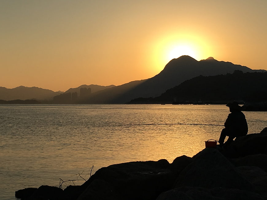 Silhouette of fisherman fishing at sunrise over Tolo Harbour