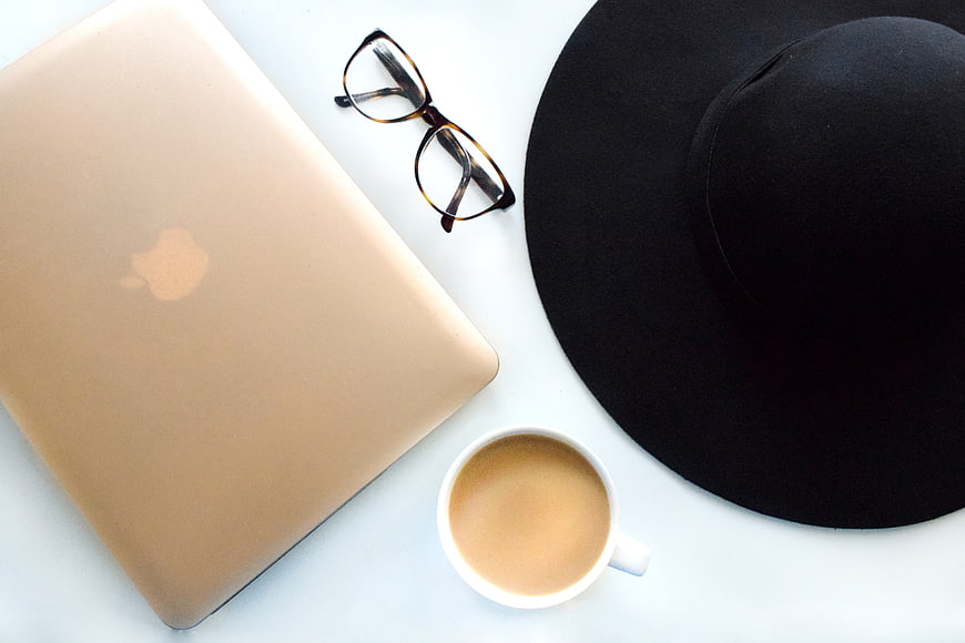 Gold laptop, black hat, glasses, and coffee cup on white background