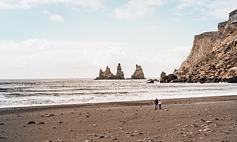 Couple walking on black sand beach with sea stacks