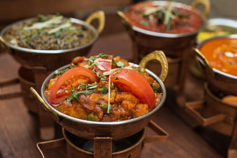 Traditional Indian curry served in copper bowls with fresh tomato garnish