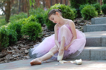 Young ballerina tying pointe shoes on outdoor steps