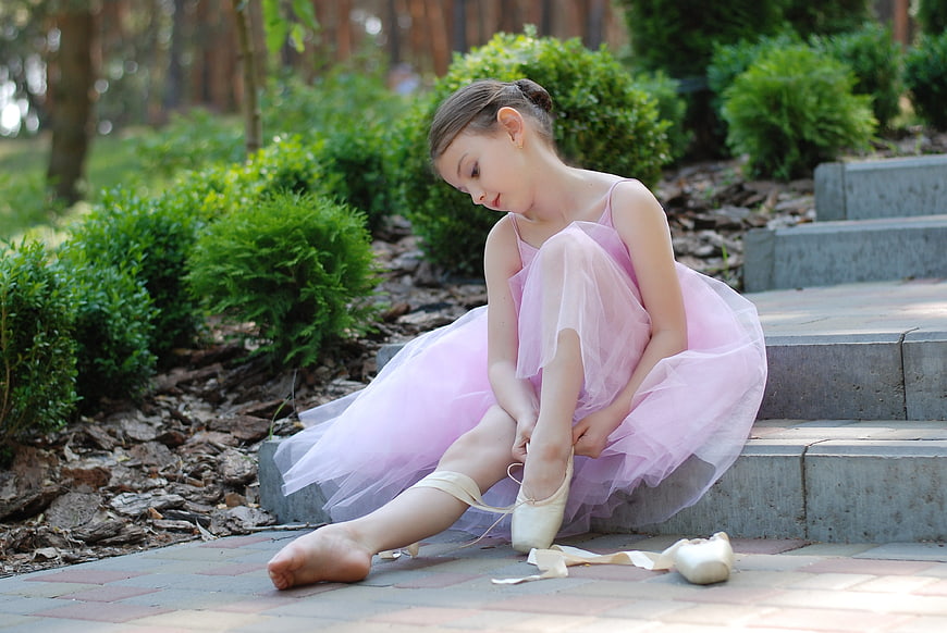 Young ballerina tying pointe shoes on outdoor steps