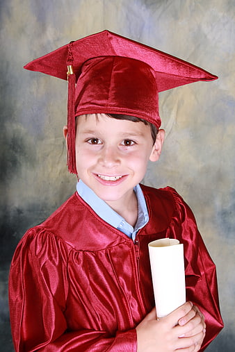 Happy young boy in red graduation cap and gown holding diploma