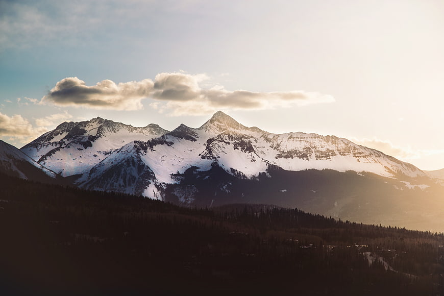 Snowy Mountain Range at Sunset with Forested Valley