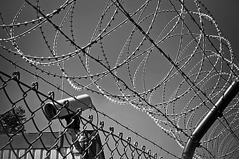 Black and white surveillance camera behind barbed wire fence