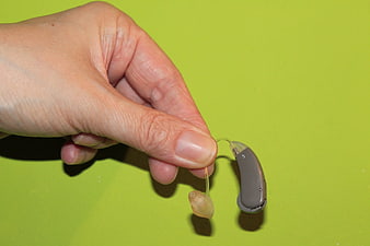 Hand Holding Gray Hearing Aid Device Against Lime Green Background