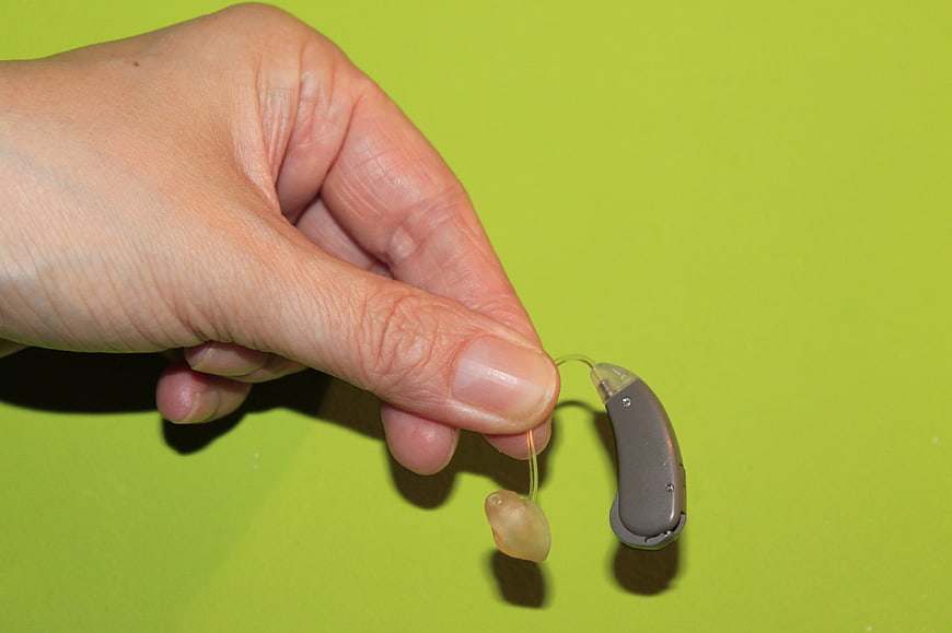 Hand Holding Gray Hearing Aid Device Against Lime Green Background