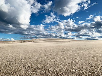 Vast sandy desert landscape under dramatic blue sky with clouds