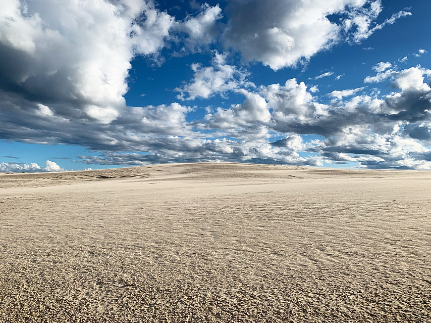 Vast sandy desert landscape under dramatic blue sky with clouds