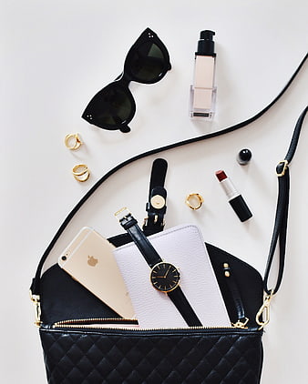 Flat lay of black handbag with accessories and makeup