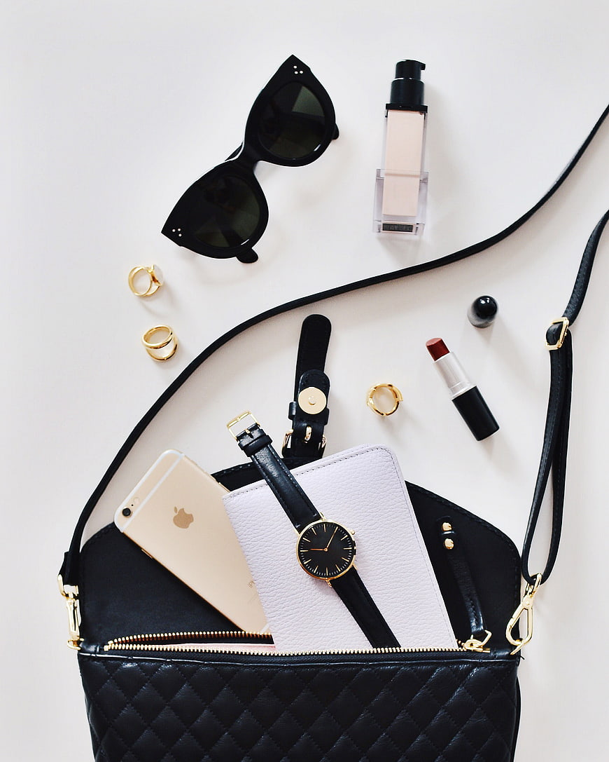 Flat lay of black handbag with accessories and makeup
