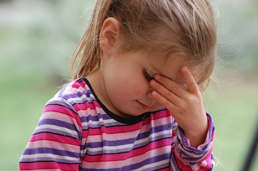 Sad little girl rubbing her eyes in striped shirt
