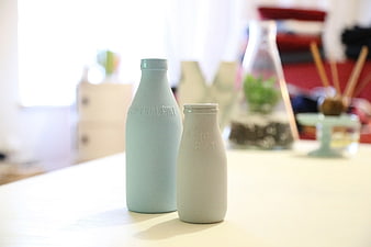 Two pastel ceramic milk bottles on a bright white table