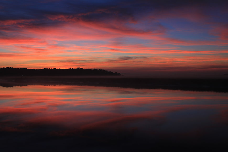 Vibrant Sunrise Reflection on Calm River with Silhouette