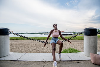 Young woman sitting on chain barrier by waterfront