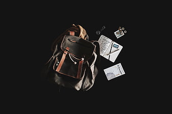 Flat lay of black backpack with travel accessories on dark background