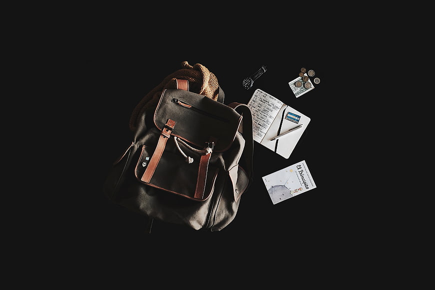 Flat lay of black backpack with travel accessories on dark background