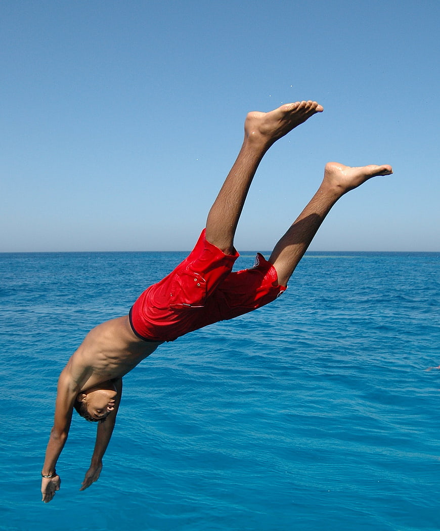 Man diving into blue ocean water mid-air
