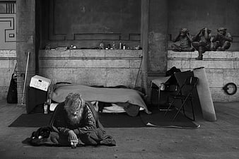 Homeless man with dog sleeping under three wise monkeys statue