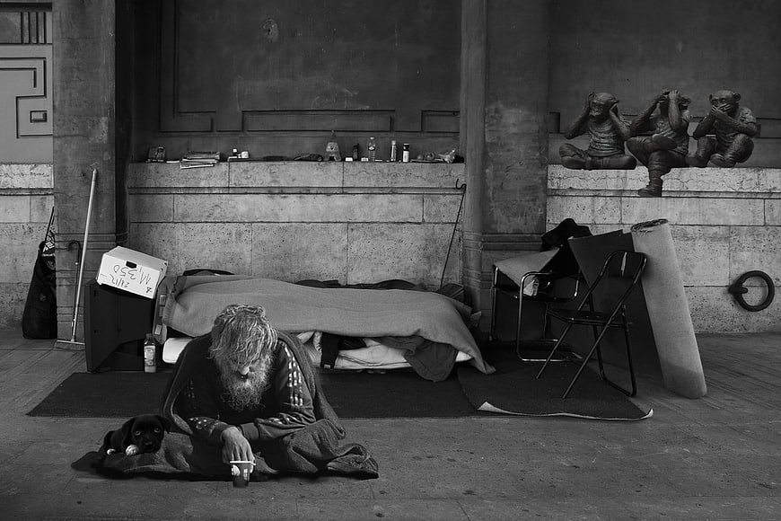Homeless man with dog sleeping under three wise monkeys statue