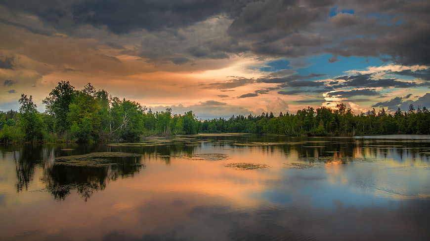 Dramatic sunset over a calm lake with forest reflections