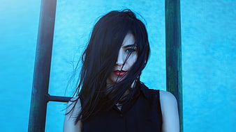 Mysterious woman with windblown hair against blue wall