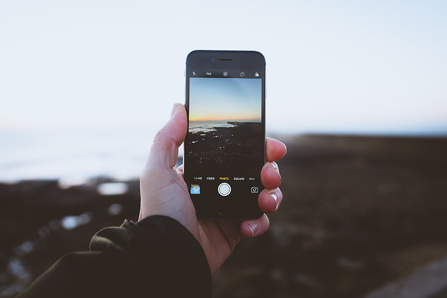 Hand holding smartphone taking photo of coastal sunset