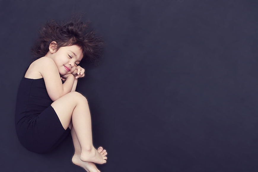 Sleeping child girl curled up on dark background
