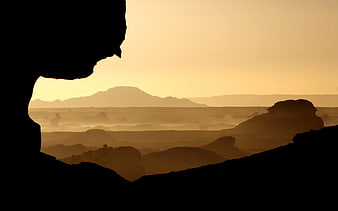 Silhouetted desert landscape viewed through a cave opening at sunset