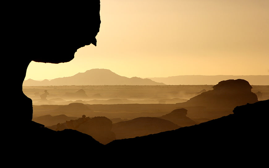 Silhouetted desert landscape viewed through a cave opening at sunset