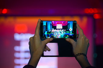 Hands holding smartphone recording event on screen