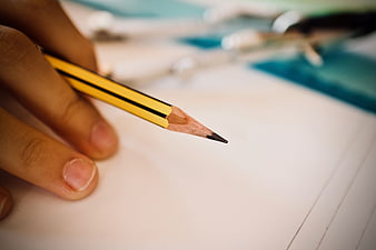 Close-up of hand holding yellow pencil over lined paper