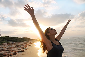 Woman with arms raised on beach at sunset
