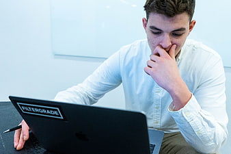 Young man thinking deeply while working on laptop in office