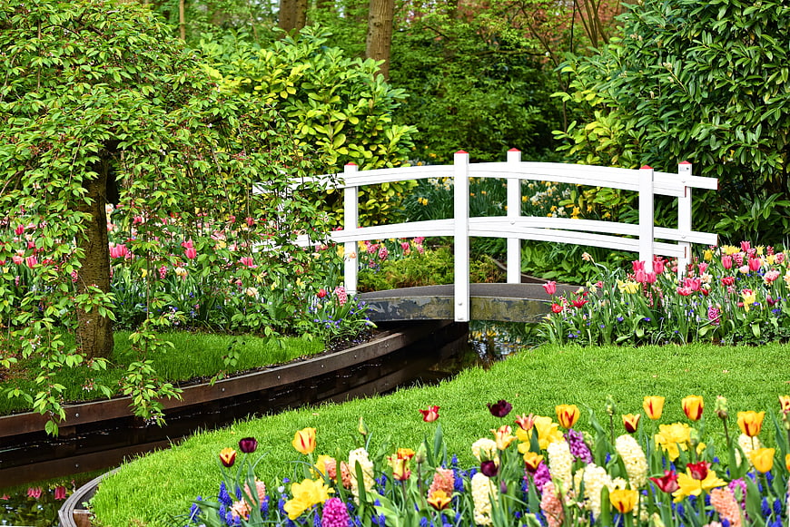 White wooden bridge over stream in vibrant spring garden