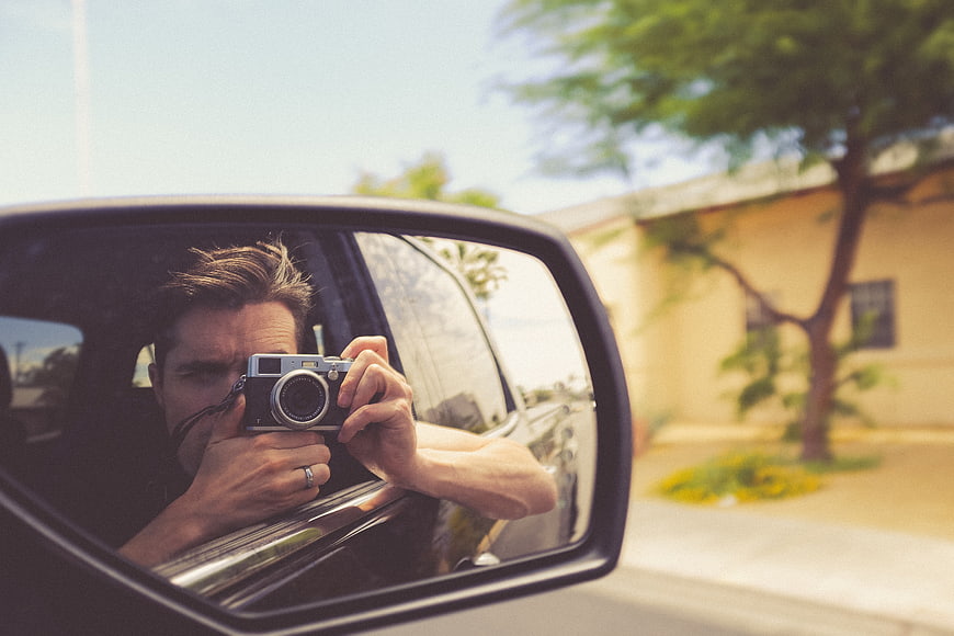 Man taking photo in car side mirror reflection