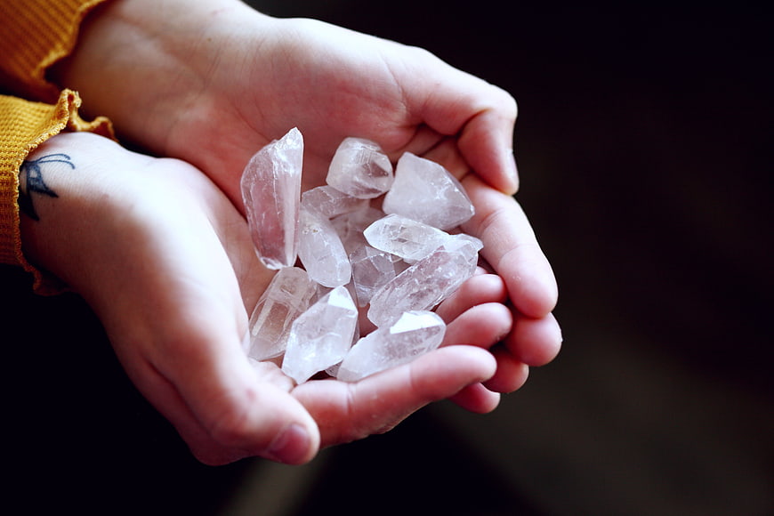 Cupped hands holding clear quartz crystals against dark background