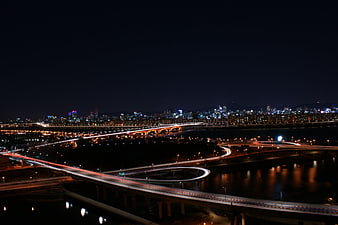 Nighttime cityscape with illuminated highway interchange and river reflections