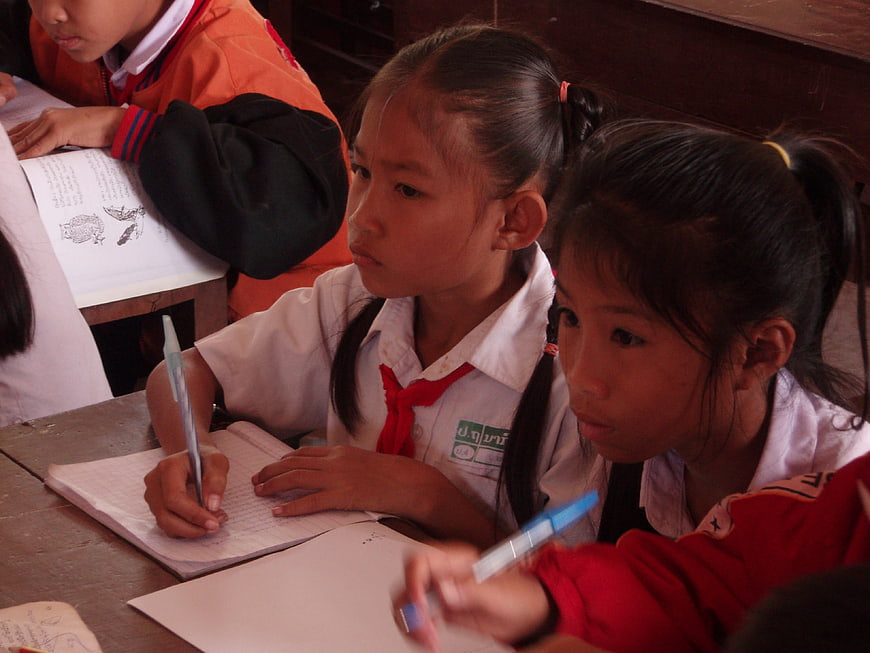 Young schoolgirls writing in notebooks during a classroom lesson in Laos