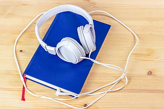 White headphones on blue book on wooden table