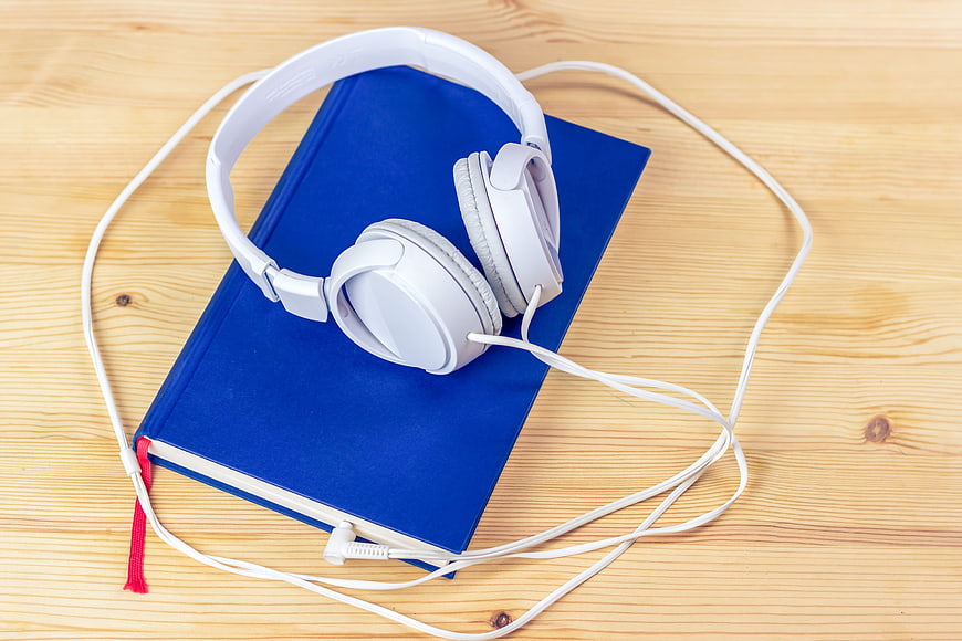 White headphones on blue book on wooden table