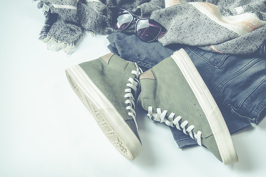 Flat lay of green sneakers, jeans, scarf, and sunglasses on white background