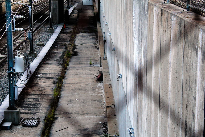Urban railway tracks alongside concrete wall and utility pole