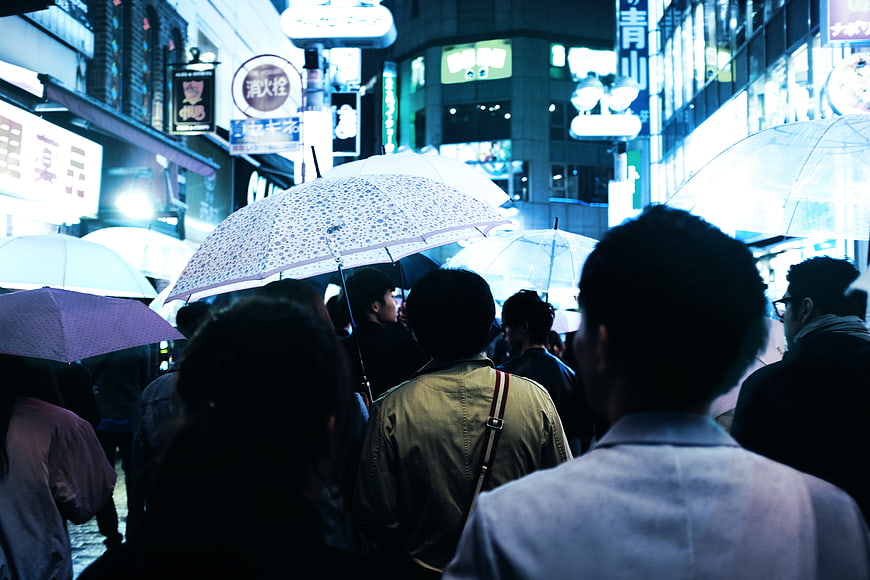 Crowd with umbrellas walking in rainy city street at night