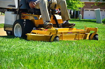 Close-up of yellow riding mower cutting green grass