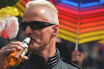 Senior man with platinum hair drinking beer at pride parade