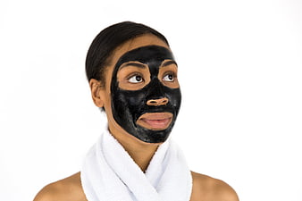 Woman with black charcoal face mask and white towel